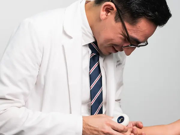 El Dr. Orozco revisa la piel del brazo de una niña con un dermatoscopio