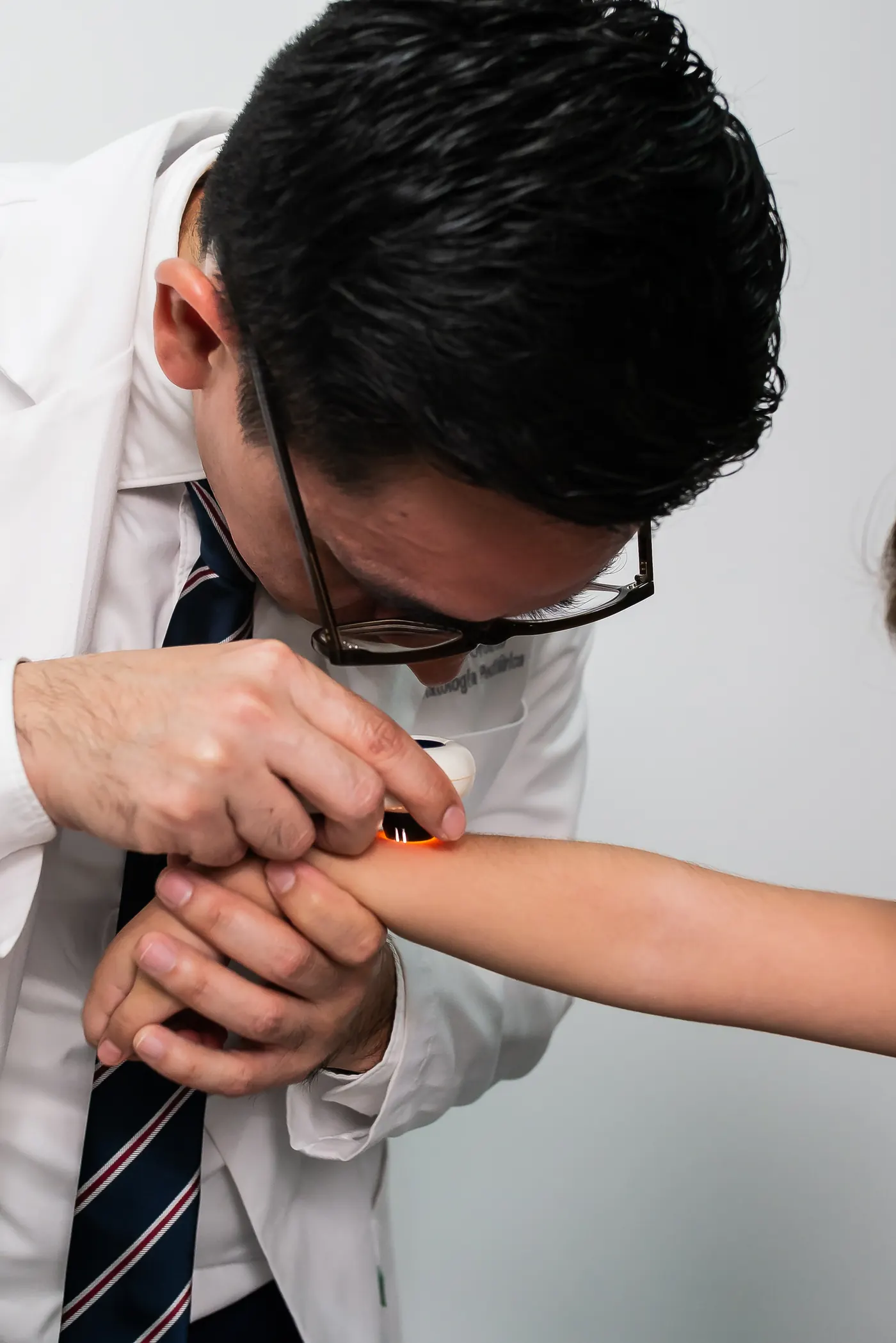 El Dr. Orozco revisa la piel del brazo de un paciente con dermatoscopio